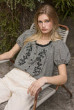 VIDA MOULIN black and white gingham blouse with floral embroidery, puff sleeves, and scoop neckline.