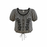VIDA MOULIN black and white gingham blouse with floral embroidery, puff sleeves, scoop neckline, and drawstring hem.