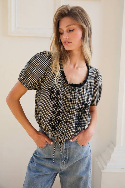 VIDA MOULIN black and white gingham blouse with floral embroidery, puff sleeves, and scoop neckline. Model wears size S.