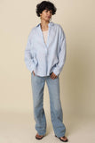 VIDA MOULIN light blue oversized linen shirt with drop shoulders, worn over a cream tank top and light wash jeans.