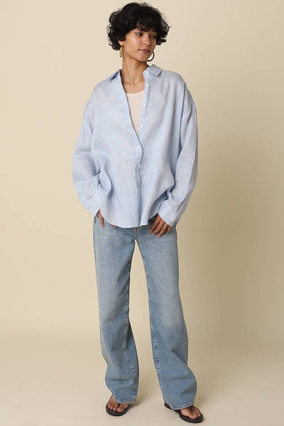 VIDA MOULIN light blue oversized linen shirt with drop shoulders, worn over a cream tank top and light wash jeans.