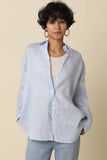 VIDA MOULIN light blue linen oversized shirt with drop shoulders worn over a cream tank top and jeans.